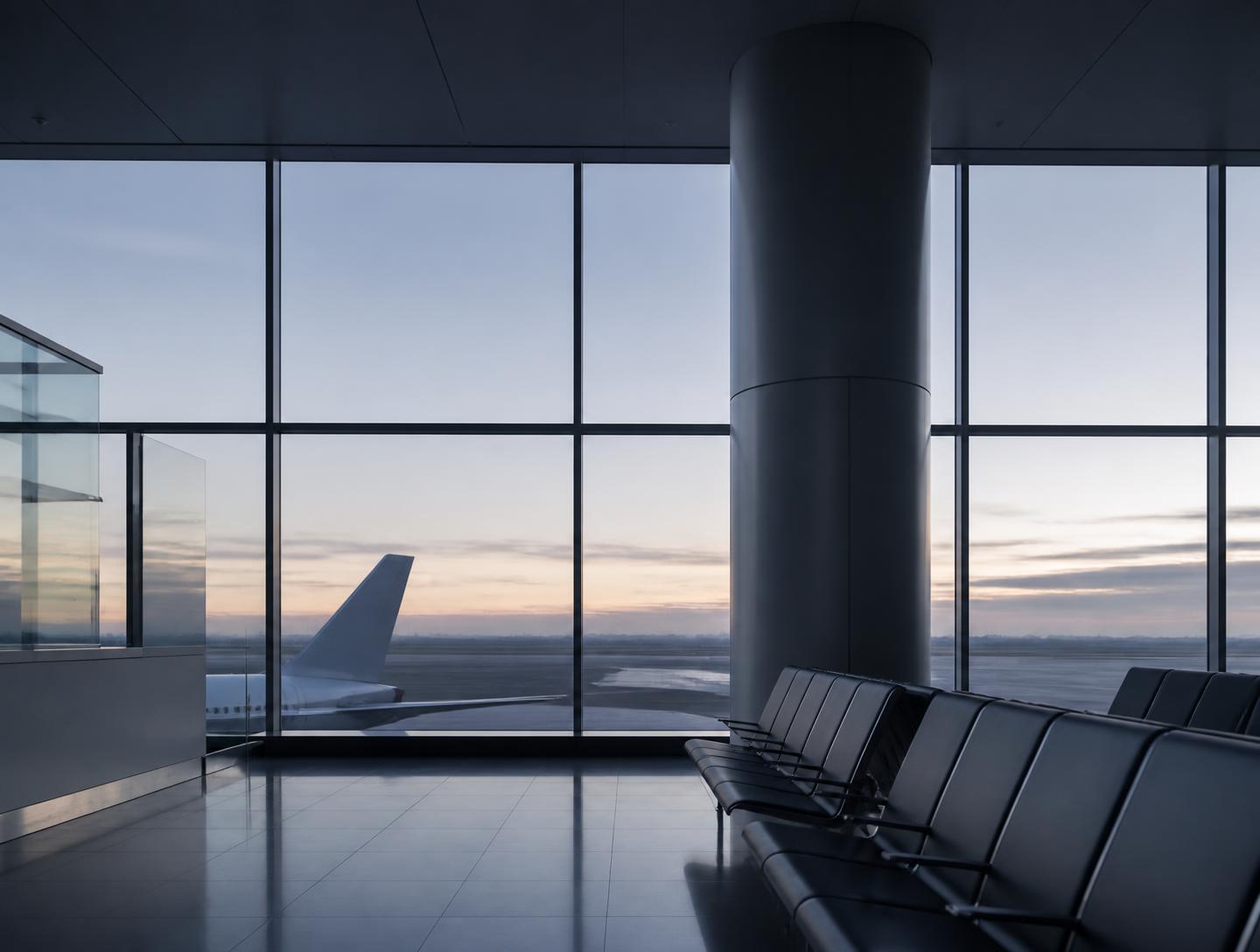 Empty airport terminal at dawn with an aircraft tail beyond the glass